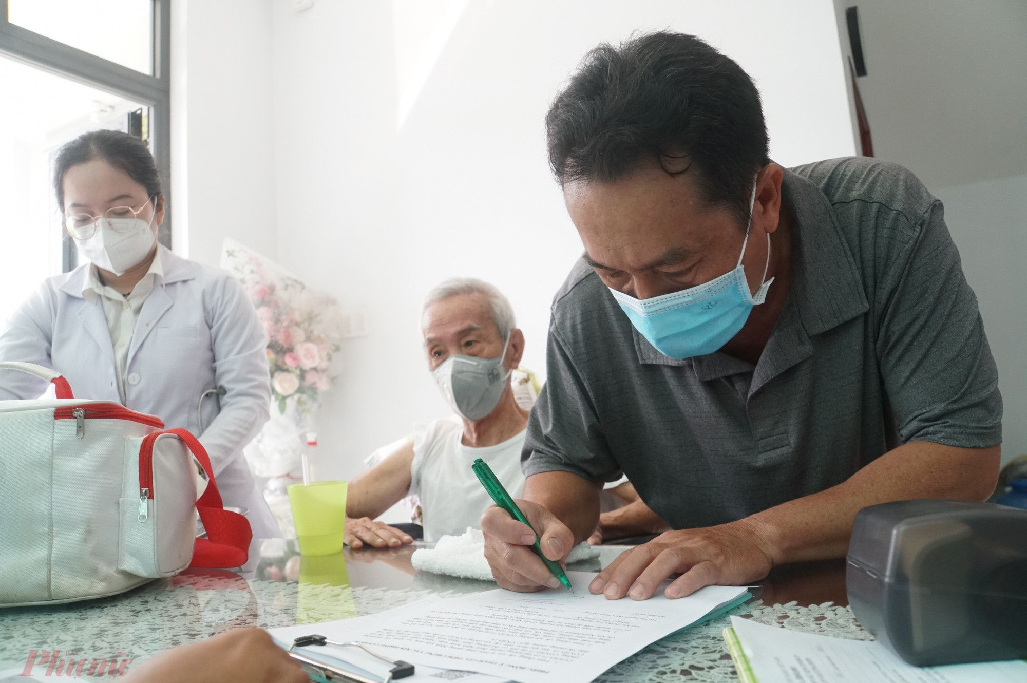 Con trai ông C. ký giấy đồng ý tiêm ngừa vắc xin cho cha, anh nói: Mũi 1 cha tôi tiêm vắc xin Pfizer ở điểm tiêm cộng đồng nhưng rất lo về lây nhiễm bệnh và sợ ông cụ bị phản ứng thuốc lắm. Lần này tôi đăng ký tiêm tại nhà, bác sĩ đến mừng lắm, đỡ nguy cơ lây nhiễm và rất tiện